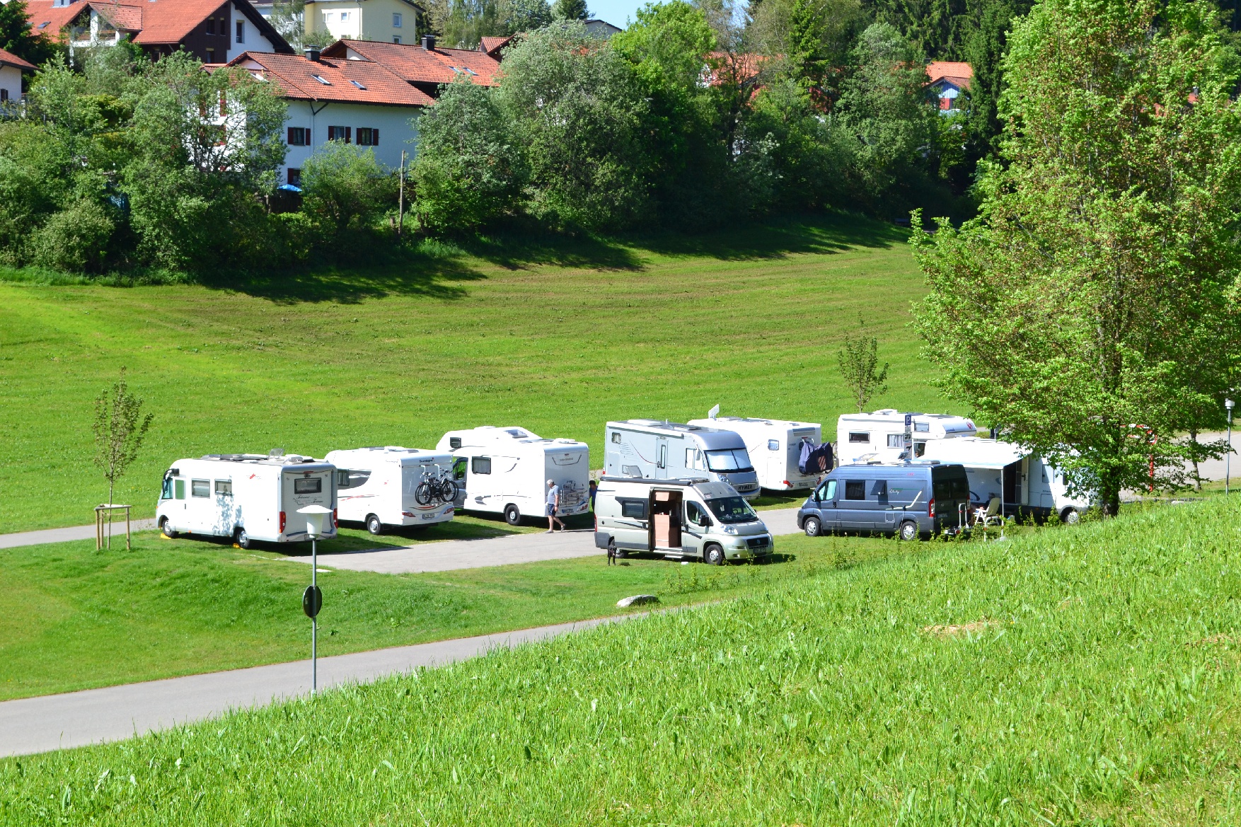 Camping-cars stationnés dans un cadre verdoyant près d'un village, ambiance paisible et nature.