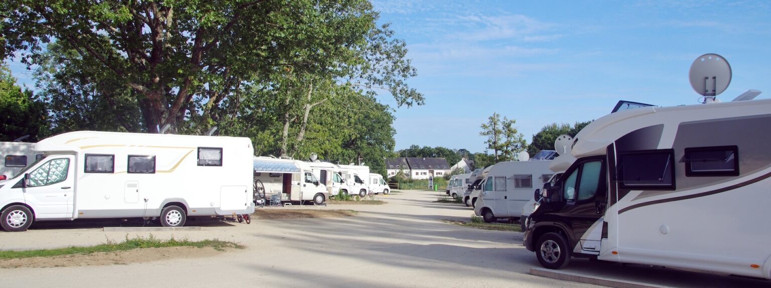Camping-cars stationnés dans un parc verdoyant sous un ciel bleu, ambiance paisible et estivale.