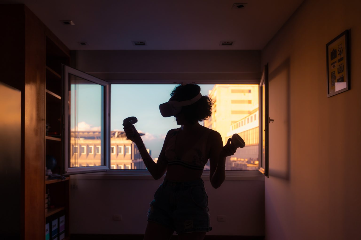 Persona con visor de realidad virtual en habitación iluminada por el atardecer, disfrutando de una experiencia inmersiva.