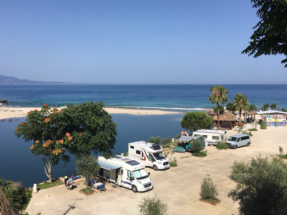 Plage et eau turquoise de Ksamil sur la Riviera albanaise avec camping-cars stationnés dans un camping.
