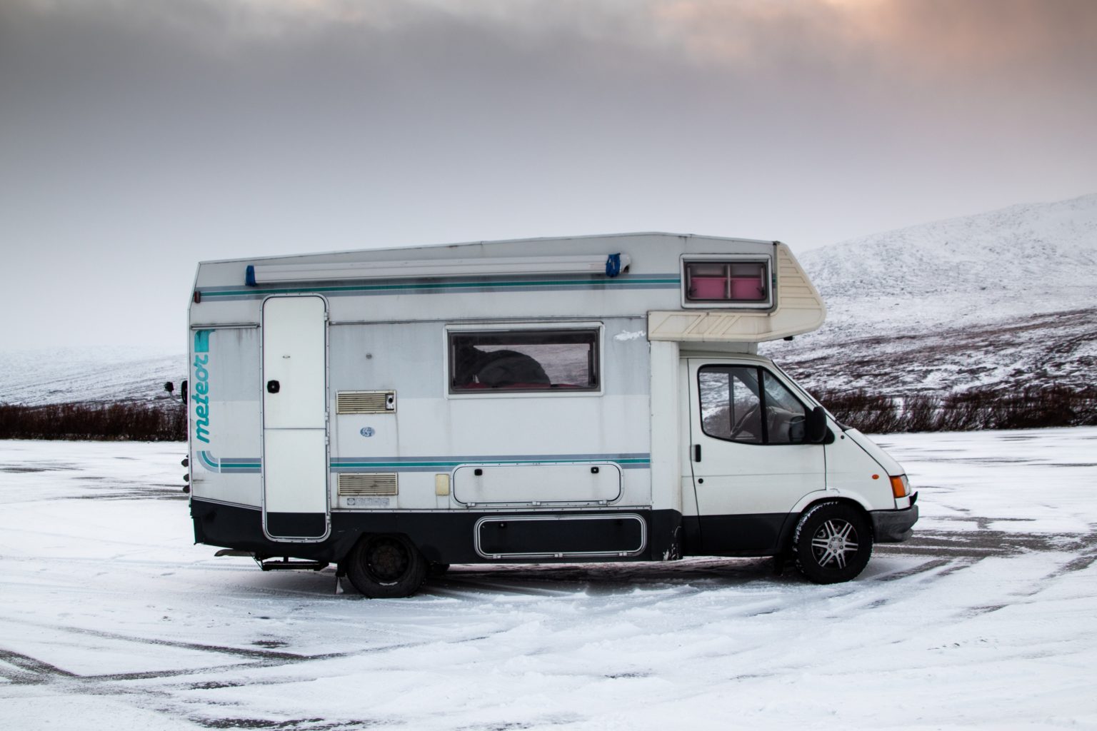 Campervan parked on a snowy landscape under a cloudy sky, evoking a sense of winter adventure and exploration.