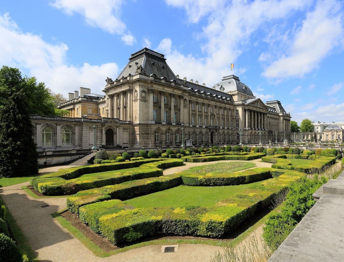 Vue du Palais royal de Bruxelles et de ses jardins à la française sous un ciel bleu.