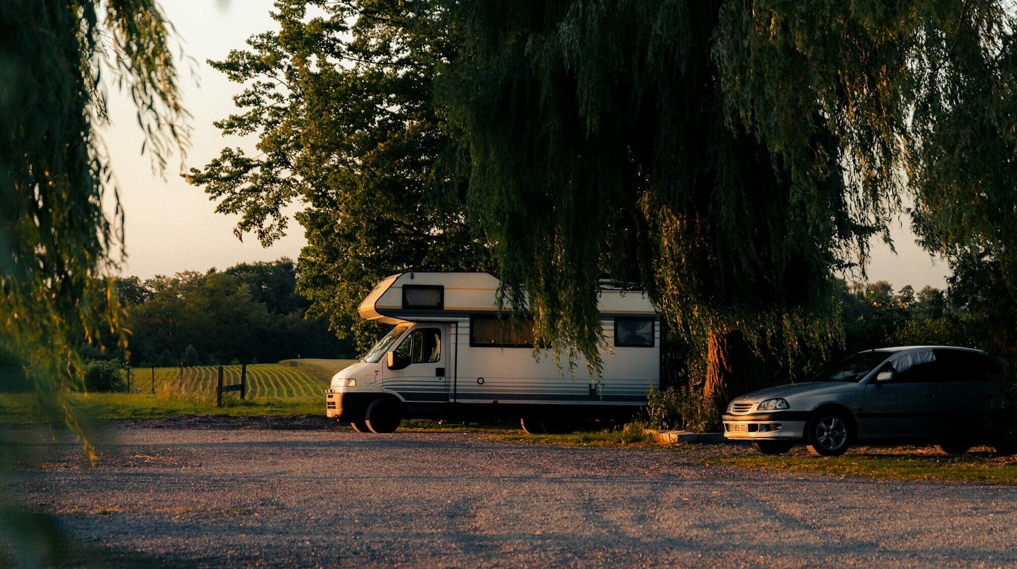 Camping-car stationné sous des arbres au coucher du soleil dans la campagne belge.