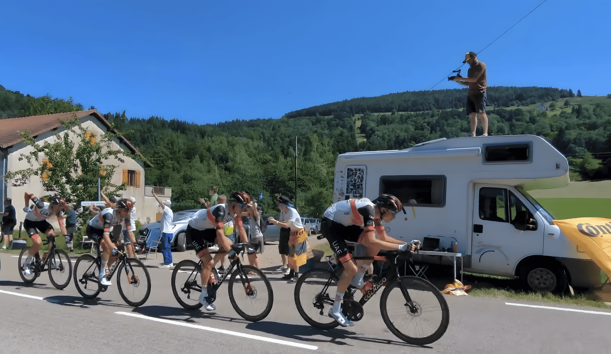Coureurs du Tour de France passant devant un camping-car et des spectateurs en montagne.