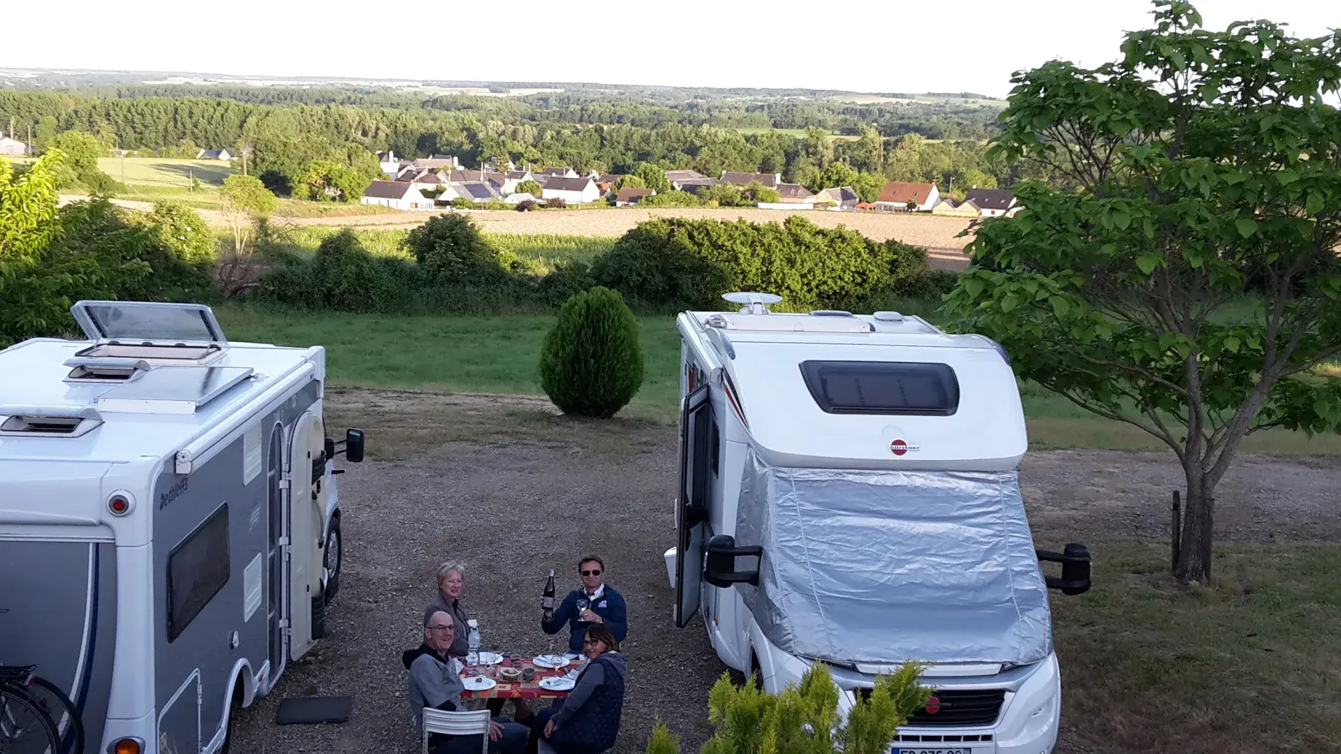 Photo de deux camping-cars avec quatre personnes mangeant autour d'une petite table entre.