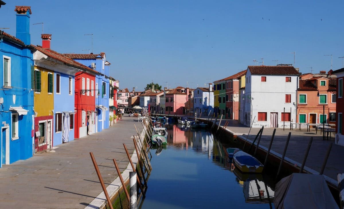 Canal calme sur l’île de Burano près de Venise, bordé de maisons colorées bleues, rouges, blanches et jaunes.