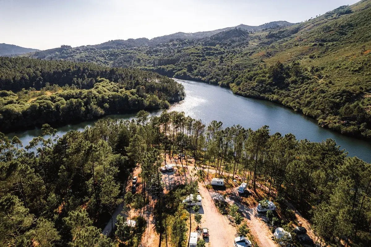 Photo aérienne d'une aire de camping pour camping-car en nature, milieu de forêt, avec un fleuve à côté.