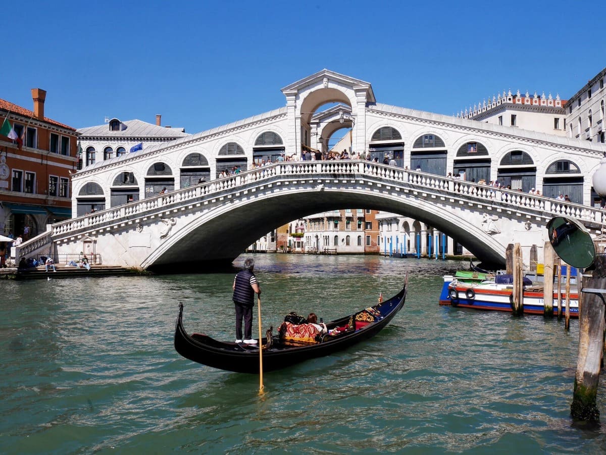 Pont du Rialto à Venise avec une gondole naviguant sur le Grand Canal sous un ciel bleu.