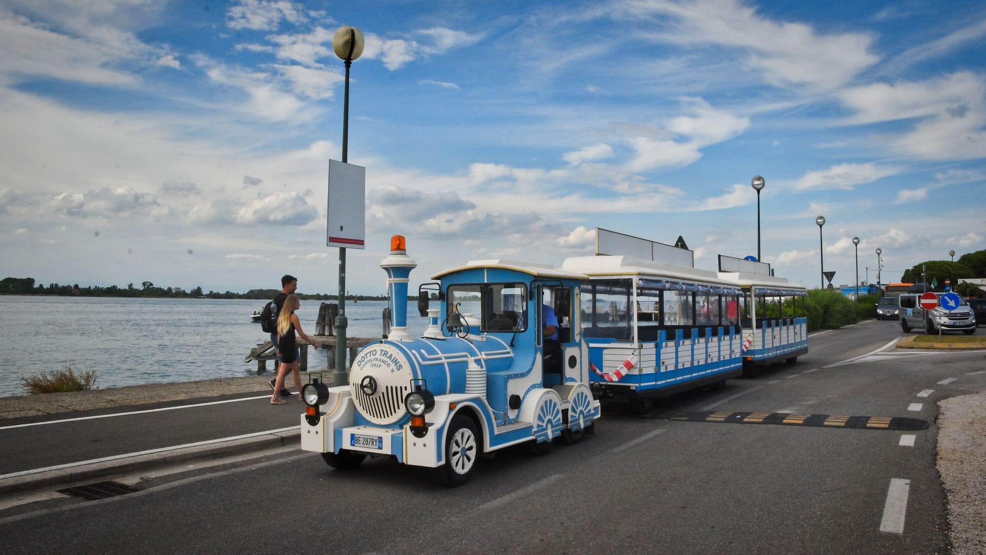 Petit train touristique bleu longeant un chemin côtier, ambiance estivale et décontractée près de l'eau.