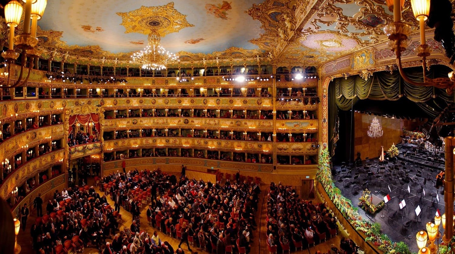 Intérieur du théâtre La Fenice à Venise avec sa salle dorée et sa scène illuminée.