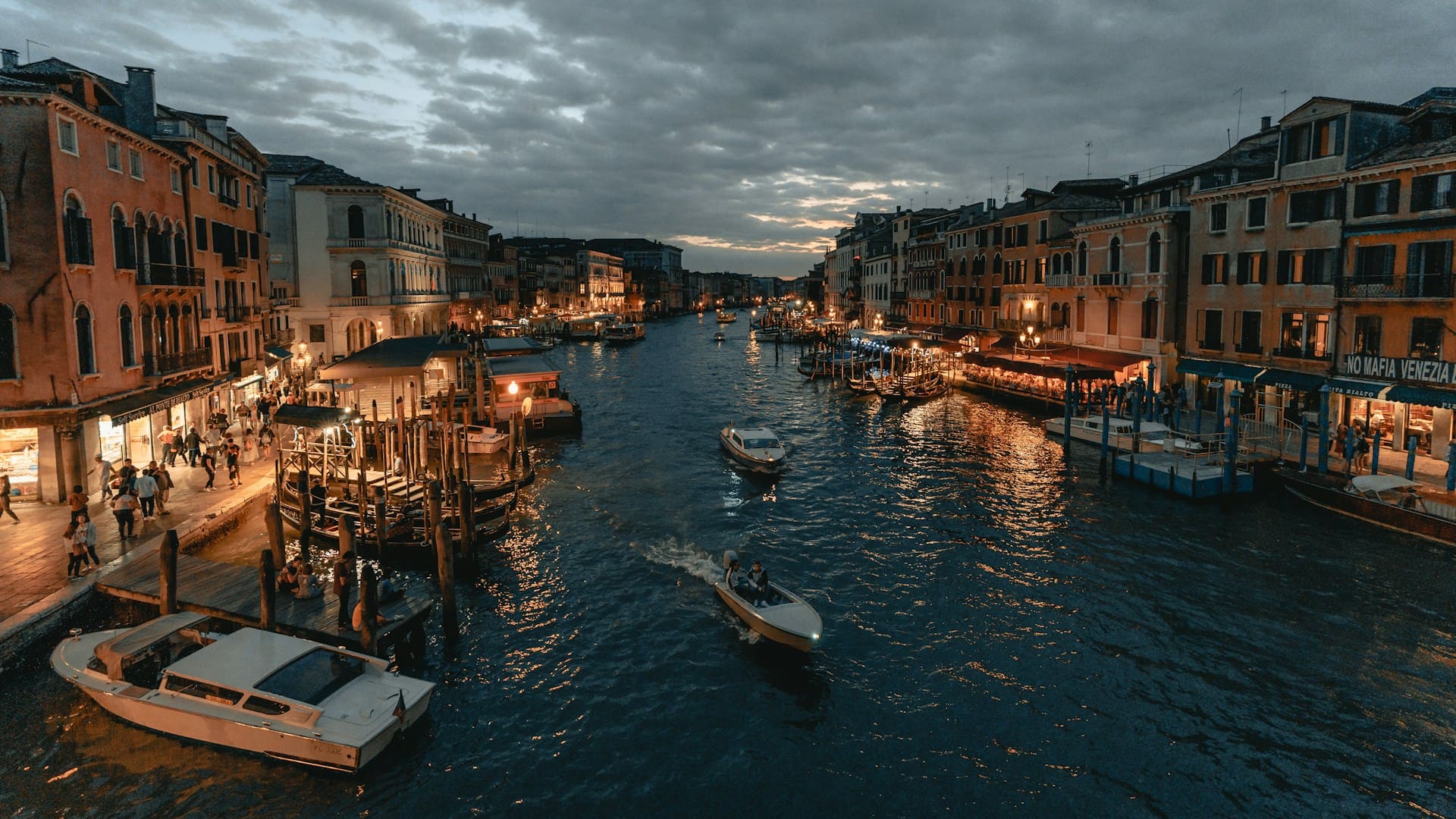 Canal animé à Venise au crépuscule, bateaux naviguant entre bâtiments éclairés, ambiance romantique et vivante.