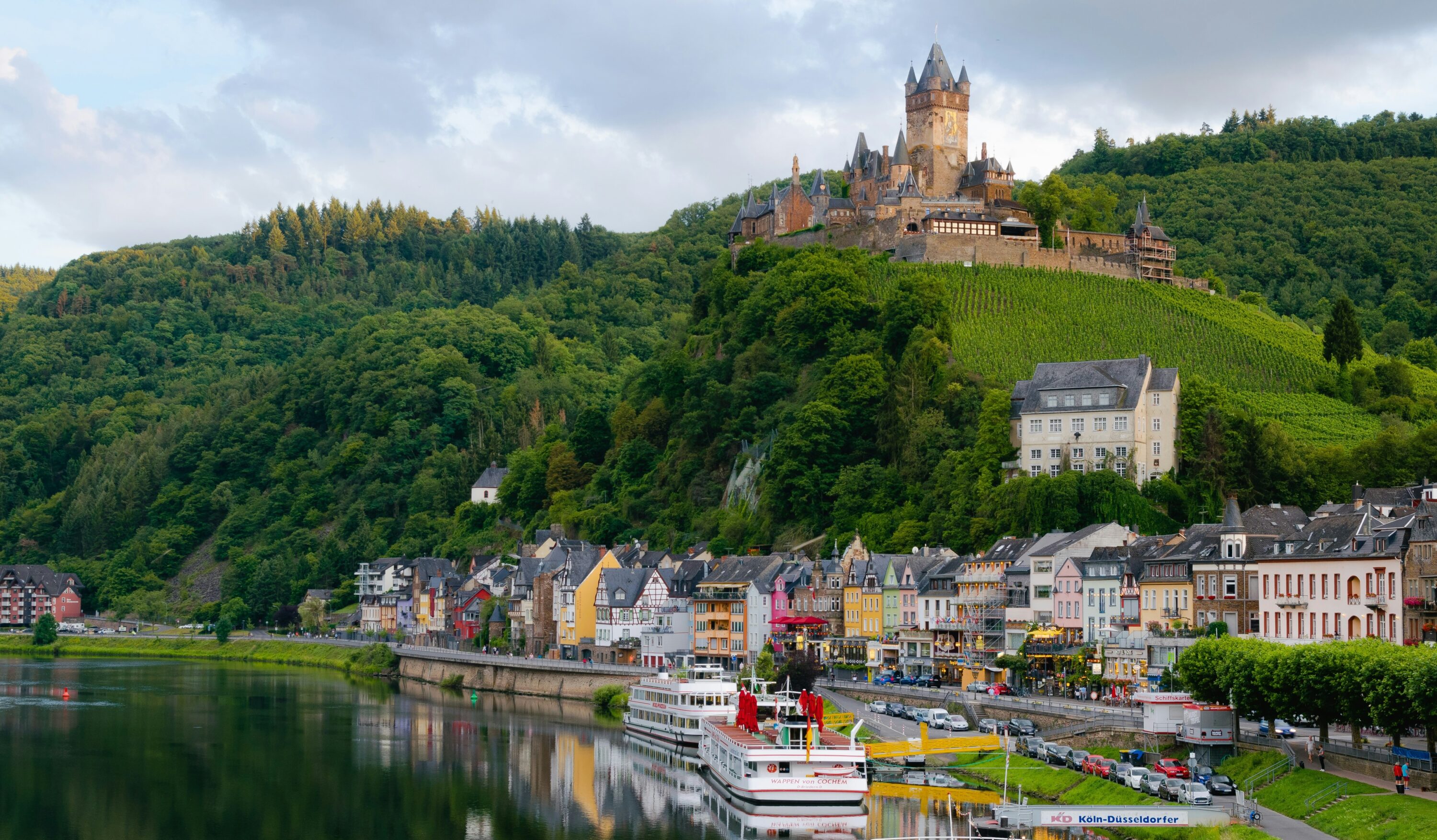 Vue sur Cochem et son château Reichsburg perché sur une colline boisée, au-dessus des maisons colorées qui bordent la Moselle, en Allemagne.